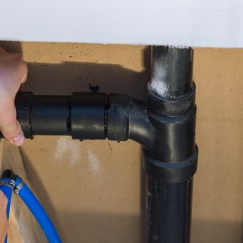 Plumber hands in glue two pieces of plastic drains PVC pipe, close up on new bathroom